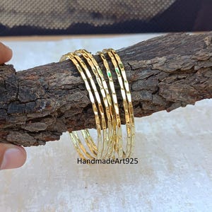 Op de afbeelding: Een set van zeven gouden armbanden met een gehamerde textuur. De armbanden zijn gestapeld op een stuk hout.