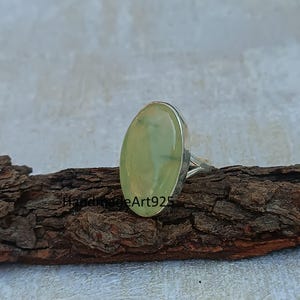 K&ouml;nnte beinhalten: Ein silberner Ring mit einem hellgr&uuml;nen ovalen Edelstein. Der Ring liegt auf einem St&uuml;ck Holz.