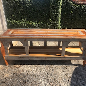 May include: A rustic wooden coffee table with a gray and brown stained finish. The table has a shelf and a decorative openwork design on the front.