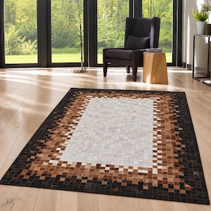 May include: A rectangular area rug featuring a mosaic pattern of small square tiles in shades of cream, tan, brown, and black. The design consists of a large central cream-colored rectangle surrounded by a multi-toned border of squares.