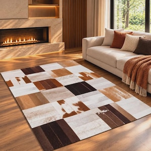 May include: A rectangular area rug featuring a patchwork design of cowhide panels in shades of white, tan, brown, and dark chocolate. The rug is composed of alternating rectangular segments with varied textures and natural hide patterns.