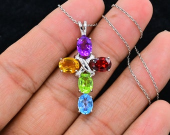 Puede incluir: Un collar de cadena de plata con un colgante de cruz con seis piedras preciosas ovaladas en un arcoíris de colores: amatista, citrino, peridoto, topacio y granate.