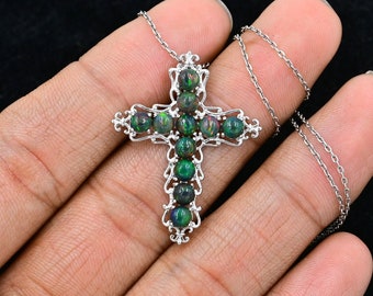 May include: A silver cross pendant necklace with a silver chain. The cross is adorned with 12 round, dark green opal gemstones.