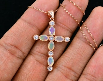 May include: A rose gold cross pendant necklace with oval-shaped opal gemstones and clear cubic zirconia accents.