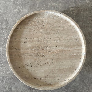 May include: A round, beige travertine serving tray with a smooth, textured surface.