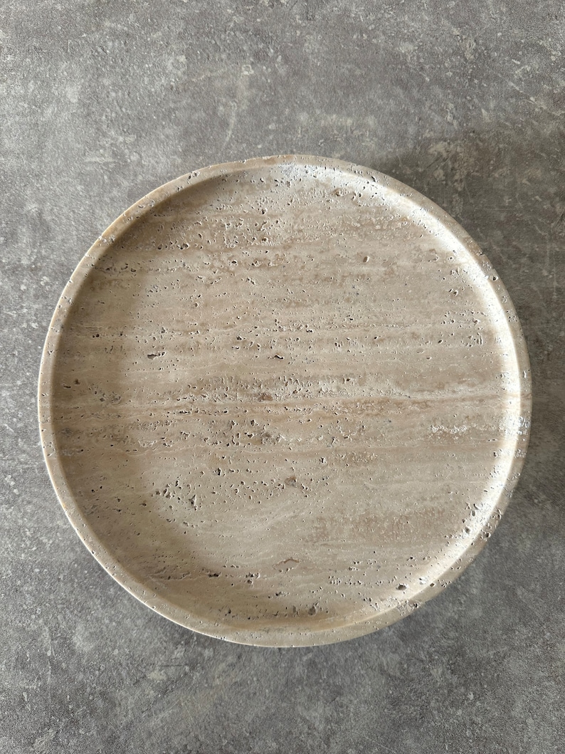 May include: A round, beige travertine serving tray with a smooth, textured surface.