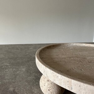 May include: A round, light beige stone tray with a raised edge. The tray is supported by three round, light beige stone balls.