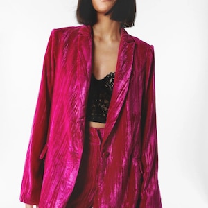 May include: A magenta velvet blazer with a single button closure and a notched lapel. The blazer has a relaxed fit and is made of a soft, luxurious fabric.