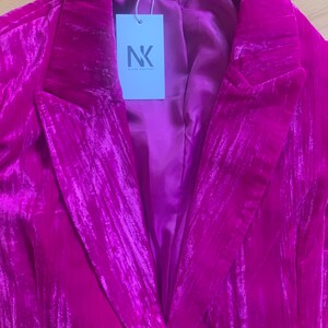 May include: A magenta velvet blazer with a notched collar and a single button closure. The blazer has a satin lining and a tag that reads "Niche Couture" and "NK Niche Couture".