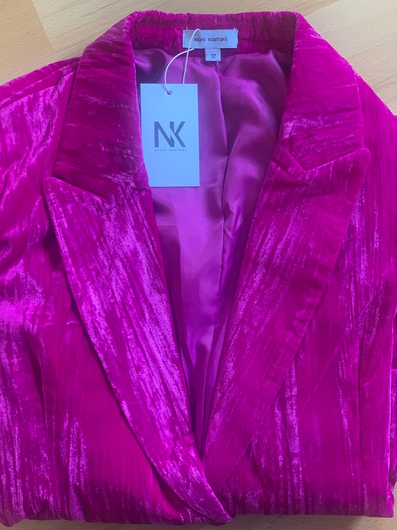 May include: A magenta velvet blazer with a notched collar and a single button closure. The blazer has a satin lining and a tag that reads "Niche Couture" and "NK Niche Couture".