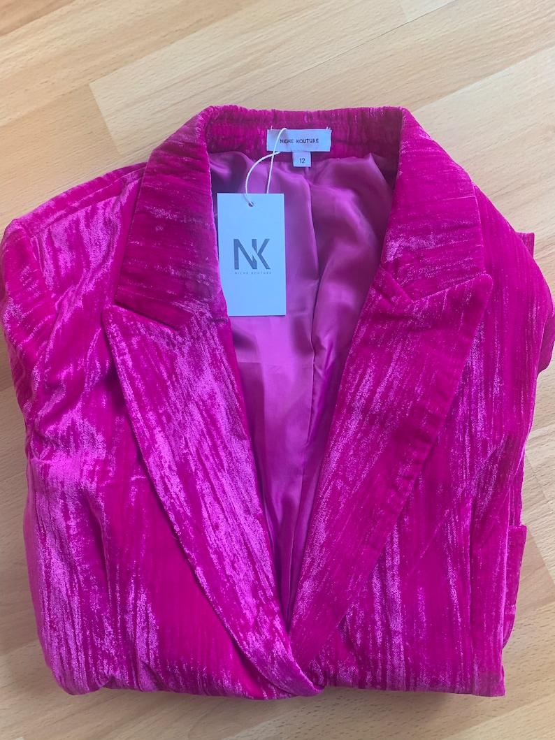 May include: A magenta velvet blazer with a notched collar and a single button closure. The blazer has a satin lining and a label that reads "Niche Couture" and "12".