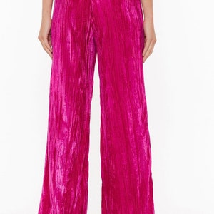 May include: Wide-leg pants in a vibrant pink crushed velvet fabric. The pants have a high waist and a relaxed fit.