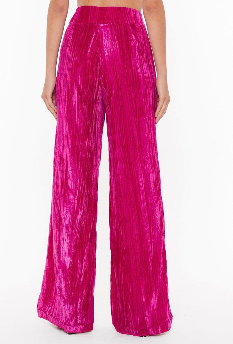 May include: Wide-leg pants in a vibrant pink crushed velvet fabric. The pants have a high waist and a relaxed fit.