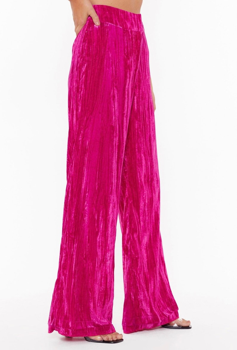 May include: Wide-leg pants in a vibrant pink crushed velvet fabric. The pants have a high waist and a relaxed fit.