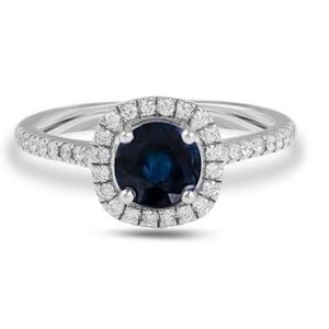 Könnte beinhalten: Ein silberner Ring mit einem runden blauen Saphir, der von einem Heiligenschein aus kleineren Diamanten umgeben ist. Die Ringschiene ist ebenfalls mit kleineren Diamanten besetzt.