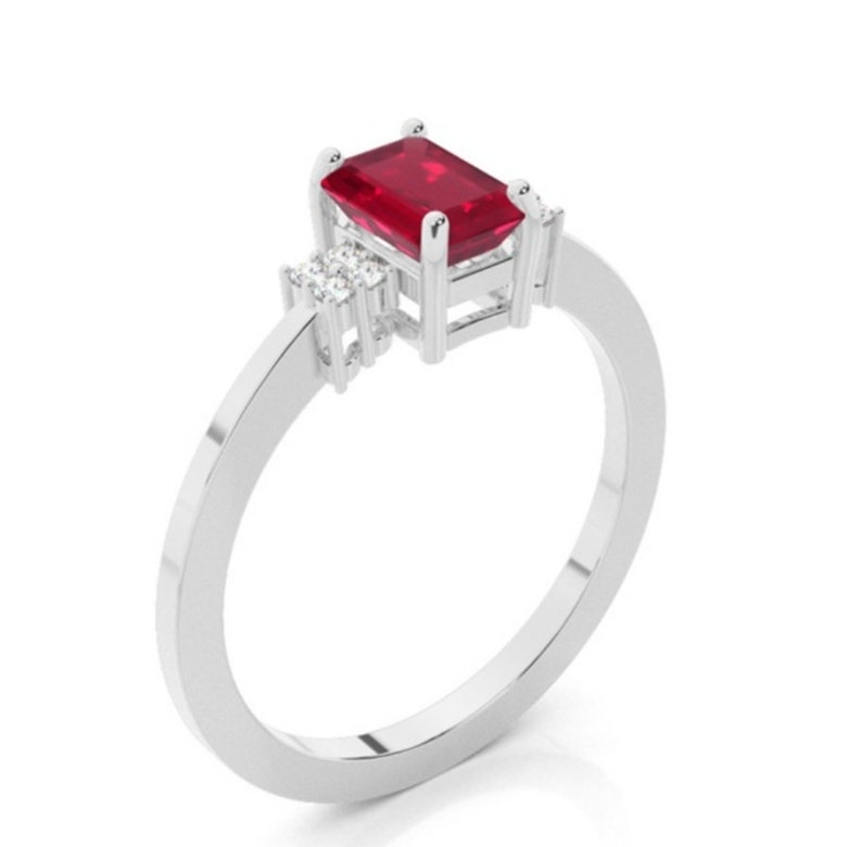 Pu&ograve; includere: Un anello d'argento con una pietra preziosa rettangolare rosso scuro come elemento principale. Due pietre preziose chiare pi&ugrave; piccole affiancano la pietra principale. L'anello ha una fascia semplice ed elegante.