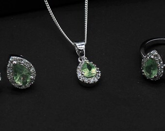 May include: A silver jewelry set with a teardrop-shaped pendant, earrings, and ring. Each piece features a green gemstone surrounded by smaller clear stones.