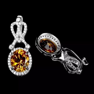 Op de afbeelding: Een paar zilveren oorbellen met een helder kristal en een bruine topaas edelsteen. De oorbellen hebben een delicaat ontwerp met een kroonvormige bovenkant en een ronde onderkant.