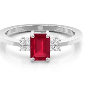 Pu&ograve; includere: Un anello d'argento con una vibrante gemma rossa rettangolare come elemento centrale. Piccoli gruppi di gemme bianche affiancano la pietra principale, aggiungendo brillantezza. La fascia &egrave; liscia e lucida, creando un design classico ed elegante.