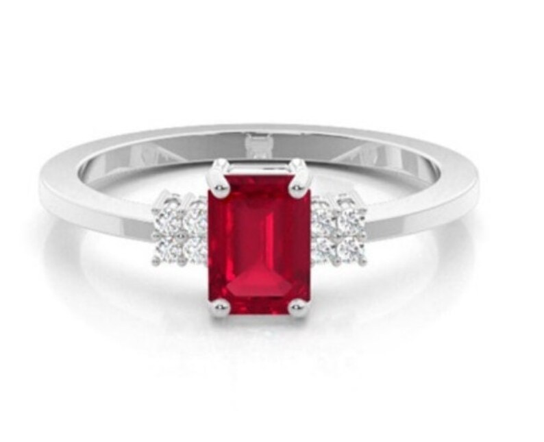 Pu&ograve; includere: Un anello d'argento con una vibrante gemma rossa rettangolare come elemento centrale. Piccoli gruppi di gemme bianche affiancano la pietra principale, aggiungendo brillantezza. La fascia &egrave; liscia e lucida, creando un design classico ed elegante.