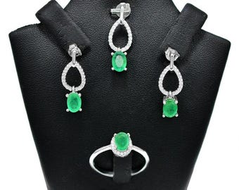 May include: A silver emerald and diamond jewelry set with a ring, earrings, and a pendant. The emerald stones are oval shaped and set in a prong setting. The earrings and pendant feature a delicate, openwork design.
