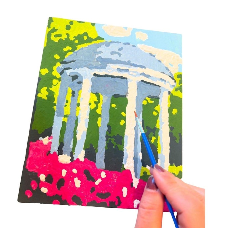 Puede incluir: Un lienzo de pintura por n&uacute;meros que representa un cenador blanco con techo azul rodeado de flores rosas. Se est&aacute; utilizando un pincel azul para pintar el cenador.