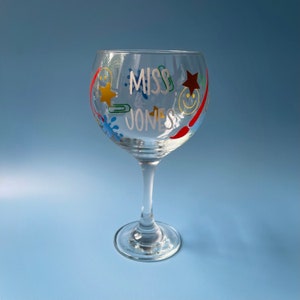 Op de afbeelding: Een helder glazen gin-glas met een wit ontwerp dat "Miss Jones" zegt en kleurrijke vormen, waaronder sterren, smiley-gezichten en verfspatten.