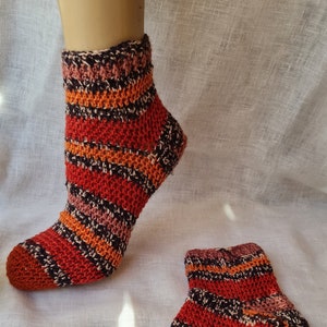 Puede incluir: Un par de calcetines tejidos a crochet con un patrón de rayas rojas, naranjas, marrones y blancas. Los calcetines son de tobillo y tienen un puño acanalado.