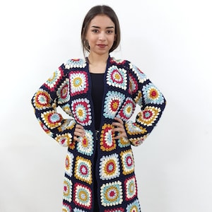 Op de afbeelding: Een lange, donkerblauwe cardigan met een gehaakt patroon met kleurrijke vierkanten. De cardigan heeft een V-hals en lange mouwen.