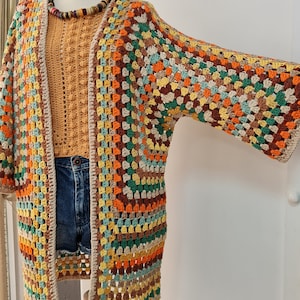 May include: A multi-colored crochet cardigan with a long, open front and three-quarter sleeves. The cardigan is made with a variety of colors, including brown, orange, yellow, green, and beige.