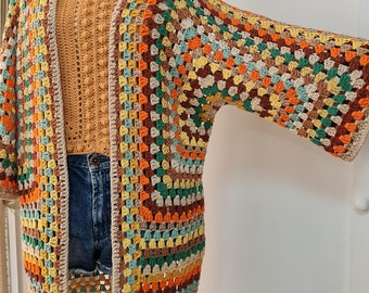 May include: A multi-colored crochet cardigan with a long, open front and three-quarter sleeves. The cardigan is made with a variety of colors, including brown, orange, yellow, green, and beige.