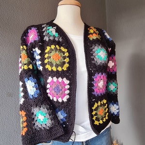 May include: A black crochet cardigan with colorful granny squares. The cardigan has a V-neck and long sleeves.