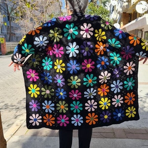 May include: A black crochet cardigan with a colorful daisy pattern. The cardigan is long and has a loose fit.