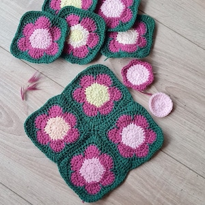 May include: A set of crocheted flower squares in shades of pink, green, and yellow. The squares are arranged in a pattern to create a larger flower design.