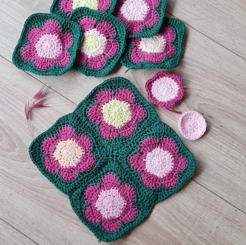 May include: A set of crocheted flower squares in shades of pink, green, and yellow. The squares are arranged in a pattern to create a larger flower design.