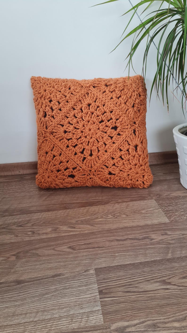 May include: A crocheted pillow with a square pattern in a burnt orange color.
