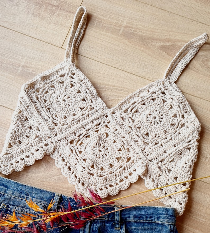 May include: A crocheted crop top with a square pattern and thin straps. The top is made of a light beige yarn and has a scalloped edge.