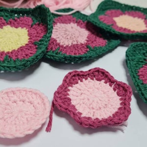 May include: A collection of crocheted flower motifs in shades of pink, green, and yellow. The motifs are made with different stitch patterns and have a variety of shapes, including circles, squares, and stars.