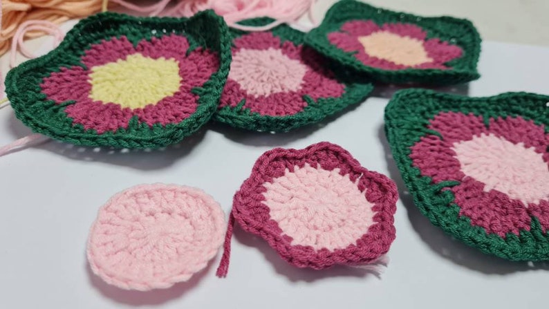 May include: A collection of crocheted flower motifs in shades of pink, green, and yellow. The motifs are made with different stitch patterns and have a variety of shapes, including circles, squares, and stars.