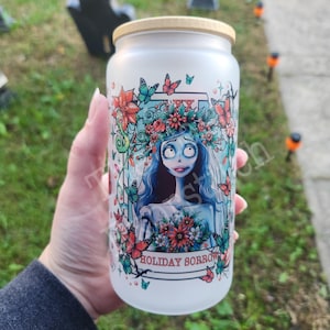 May include: A white frosted glass jar with a wooden lid featuring a colorful illustration of a character with a floral crown and the text "HOLIDAY SORROW".