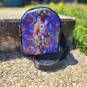 May include: A black and blue mini backpack with a graphic print of a character from the movie Beetlejuice. The backpack has a black adjustable strap.