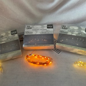 Könnte beinhalten: Drei Packungen LED-Kupfer- und Silberdraht-Lichterketten. Jede Packung enthält 30 LED-Leuchten und ist 3 Meter lang. Die Packungen sind mit "Luca Lighting" gekennzeichnet und tragen den Hinweis "Indoor".