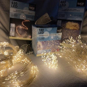 Könnte beinhalten: Drei Boxen mit LED-Lichterketten, jede mit einer anderen Anzahl von Lichtern: 520, 480 und 180. Die Boxen stehen auf einer weißen Oberfläche, im Vordergrund liegt ein Knäuel Lichterketten.