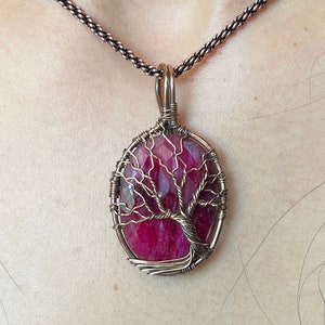 Può includere: Una collana con un ciondolo in filo di rame avvolto attorno a una pietra preziosa rossa con un design ad albero della vita.