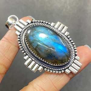 May include: A silver pendant featuring a large oval-shaped blue labradorite gemstone set in a silver bezel. The pendant has a detailed silver design around the stone and a silver bail.