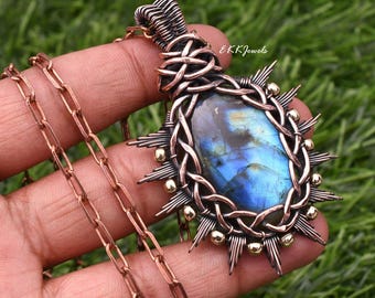 May include: A pendant necklace featuring an oval labradorite gemstone with blue iridescence, encased in intricate copper wire wrapping with small metallic beads. The pendant hangs from a matching copper chain, and the text EKKJewels is visible.
