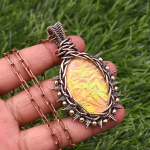 May include: A copper wire wrapped pendant necklace with a yellow iridescent glass oval stone. The pendant is accented with gold beads and copper wire spikes.