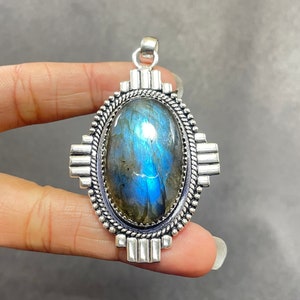 May include: A silver pendant featuring a large oval labradorite gemstone set within a silver frame. The frame has a geometric design with intricate details.