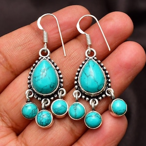 May include: Turquoise dangle earrings with a teardrop-shaped stone and smaller round stones. The earrings are made of silver and have a bohemian style.