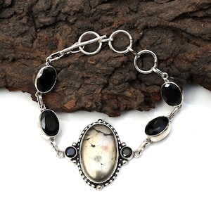 May include: Silver bracelet with a large oval-shaped gemstone and smaller black gemstones. The bracelet has a toggle clasp.